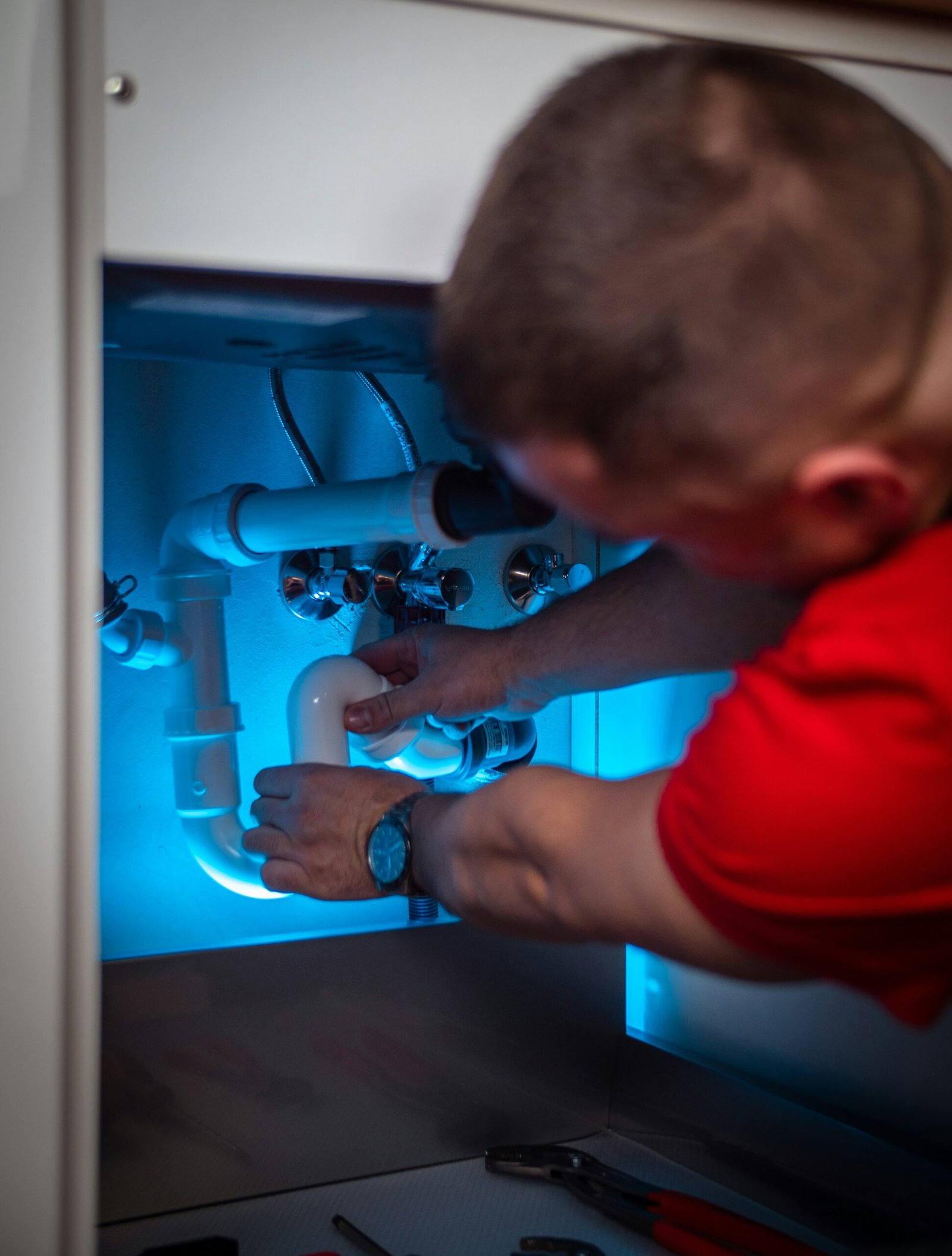 Plumber repairing pipes under a kitchen cabinet, Aurora, CO