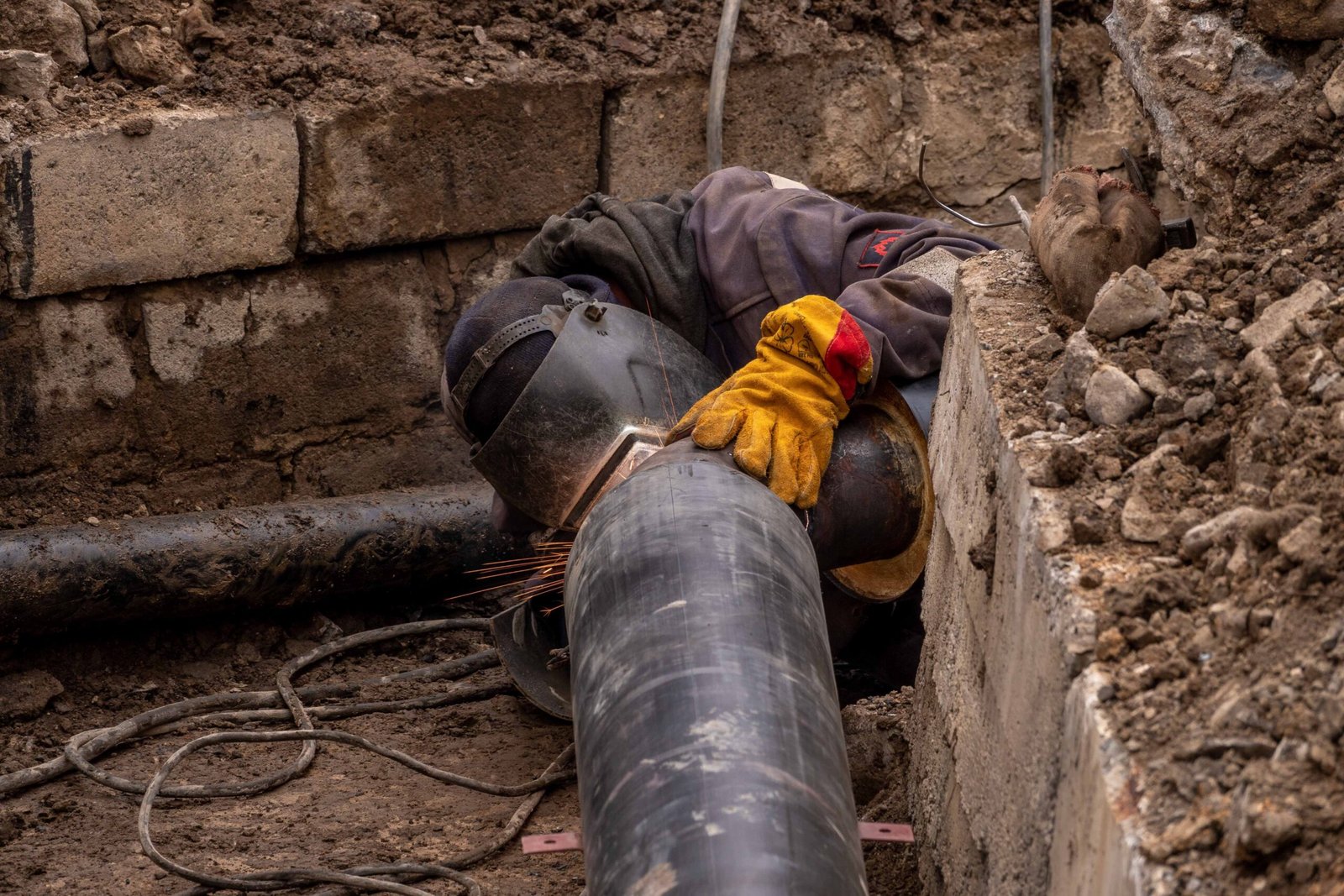 Worker repairing a steel sewer pipe in an outdoor trench, Aurora, CO